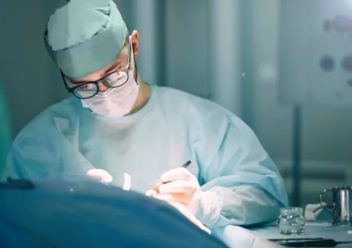 A surgeon in scrubs and a mask performs surgery.
